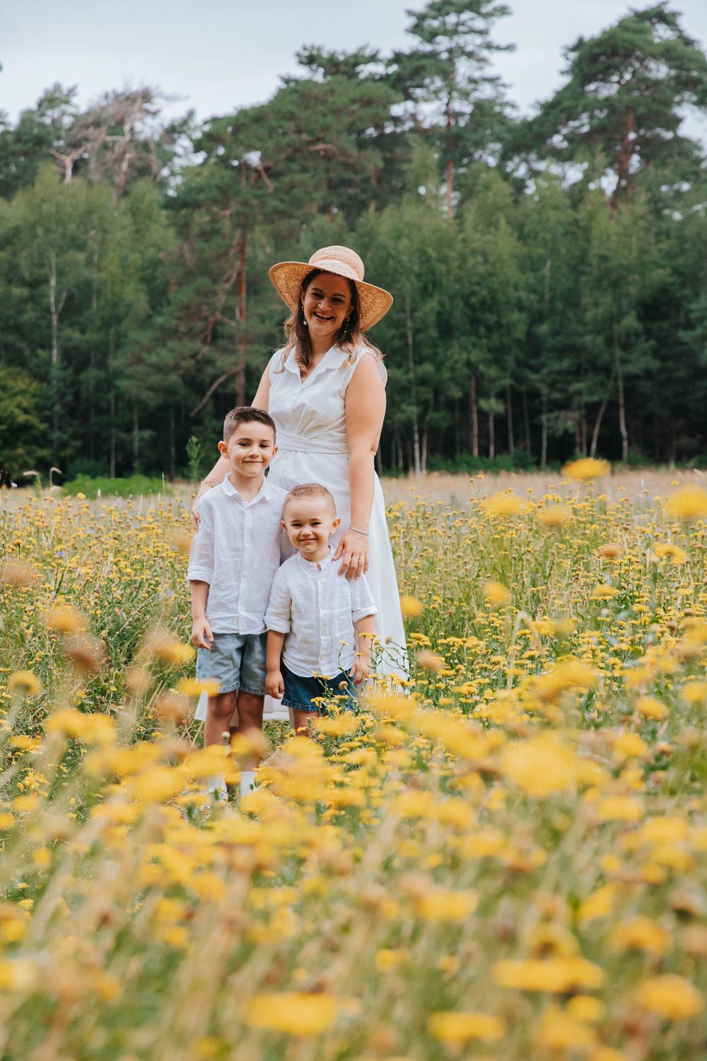 People in white clothing stand together in a vibrant yellow wildflower meadow with tall pine trees in the background.