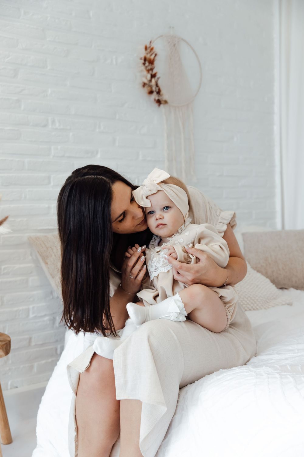A mother and baby share tender moments together on a white couch against a brick wall background.