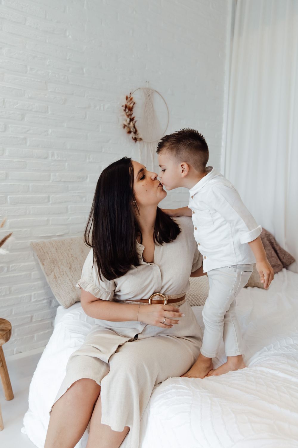 Sweet tender moment captured in white bedroom with neutral tones and brick walls showing loving interaction.