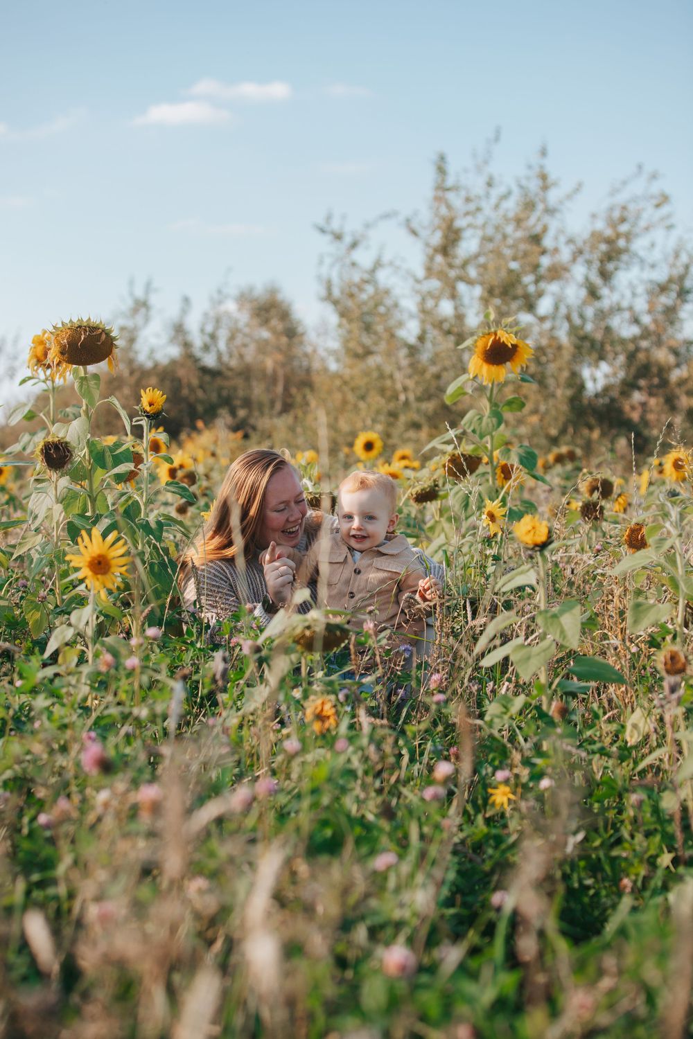 Two people share a joyful moment surrounded by tall blooming sunflowers in a summer field.