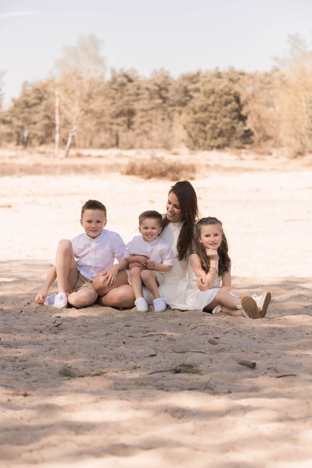 A family in white clothing poses together on a sandy beach during a warm sunset photo session.