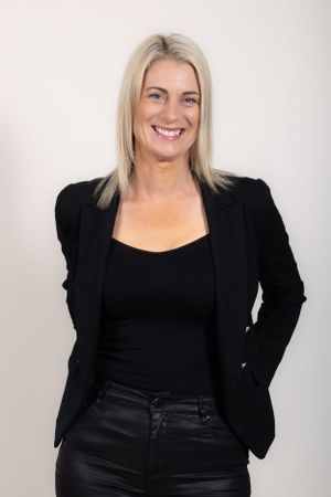Professional portrait of someone in a black blazer and top against a light background.