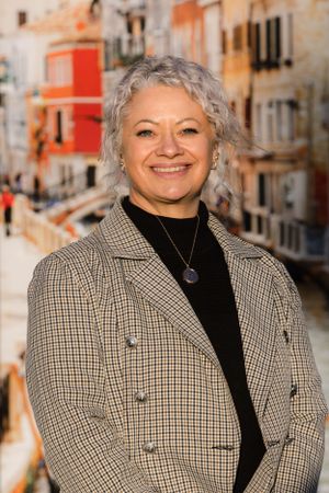 Professional headshot of a person in a plaid blazer and black top against a colorful urban background.