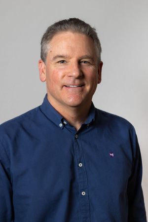 Professional headshot of a person wearing a navy button-down shirt against a studio backdrop.