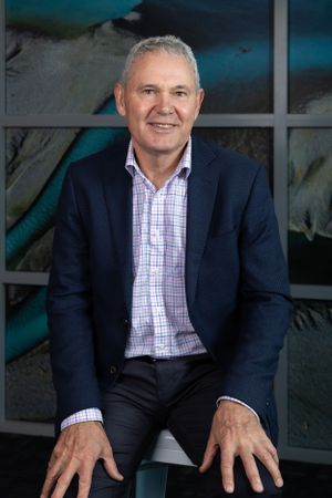 Professional portrait of a person in a navy blazer and checkered shirt against an artistic backdrop.