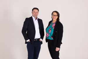 Two professionals posing together against a light background in business attire.
