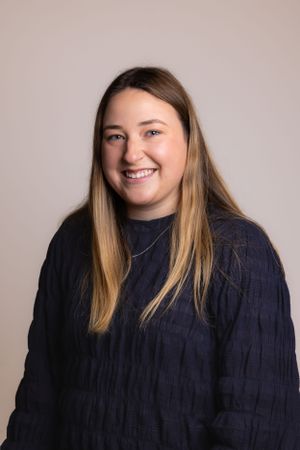 Portrait of a person wearing a navy sweater against a neutral background.
