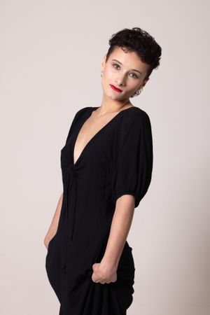 Fashion portrait of someone in a stylish black jumpsuit with puff sleeves posing against a light backdrop.