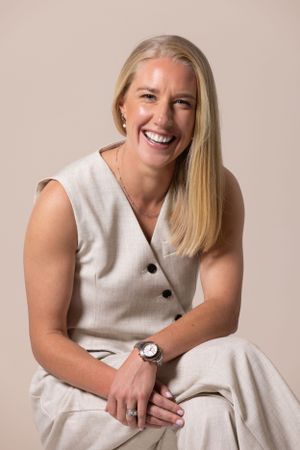 A person wearing a sleeveless white dress sits casually while displaying a bright, joyful smile.
