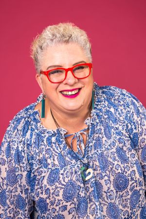 Vibrant portrait of person in blue floral top and red glasses against pink background.