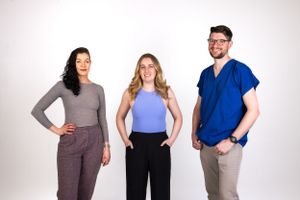 Three professionals pose together against white background in business casual attire.