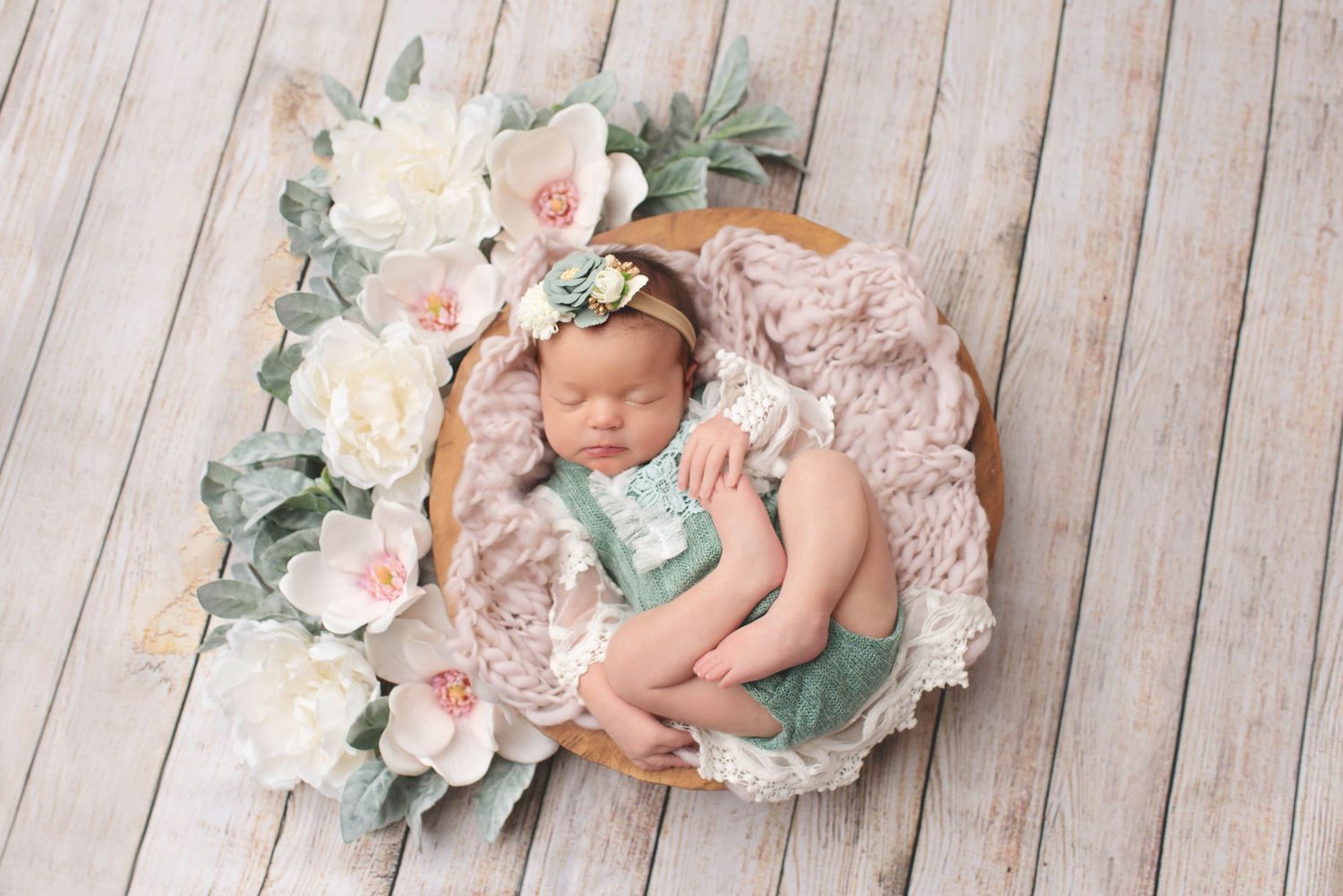 newborn baby girl with flowers and greenery on wood backdrop