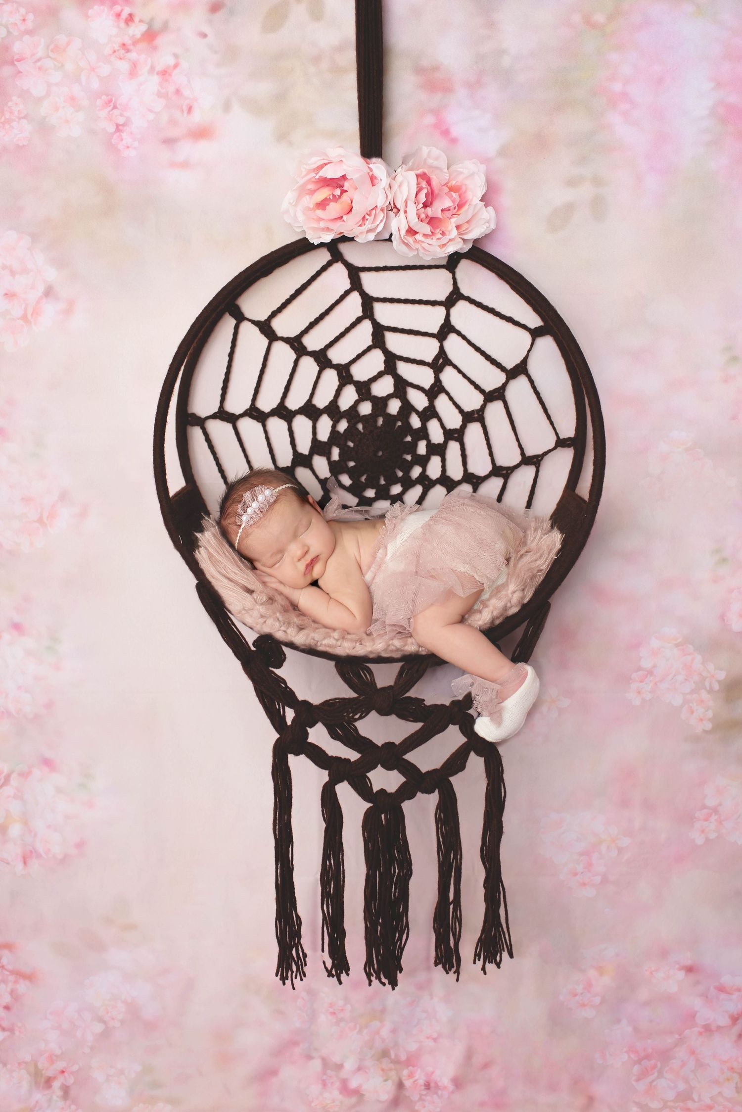 newborn baby girl in dreamcatcher swing with pink flowers and pink floral backdrop