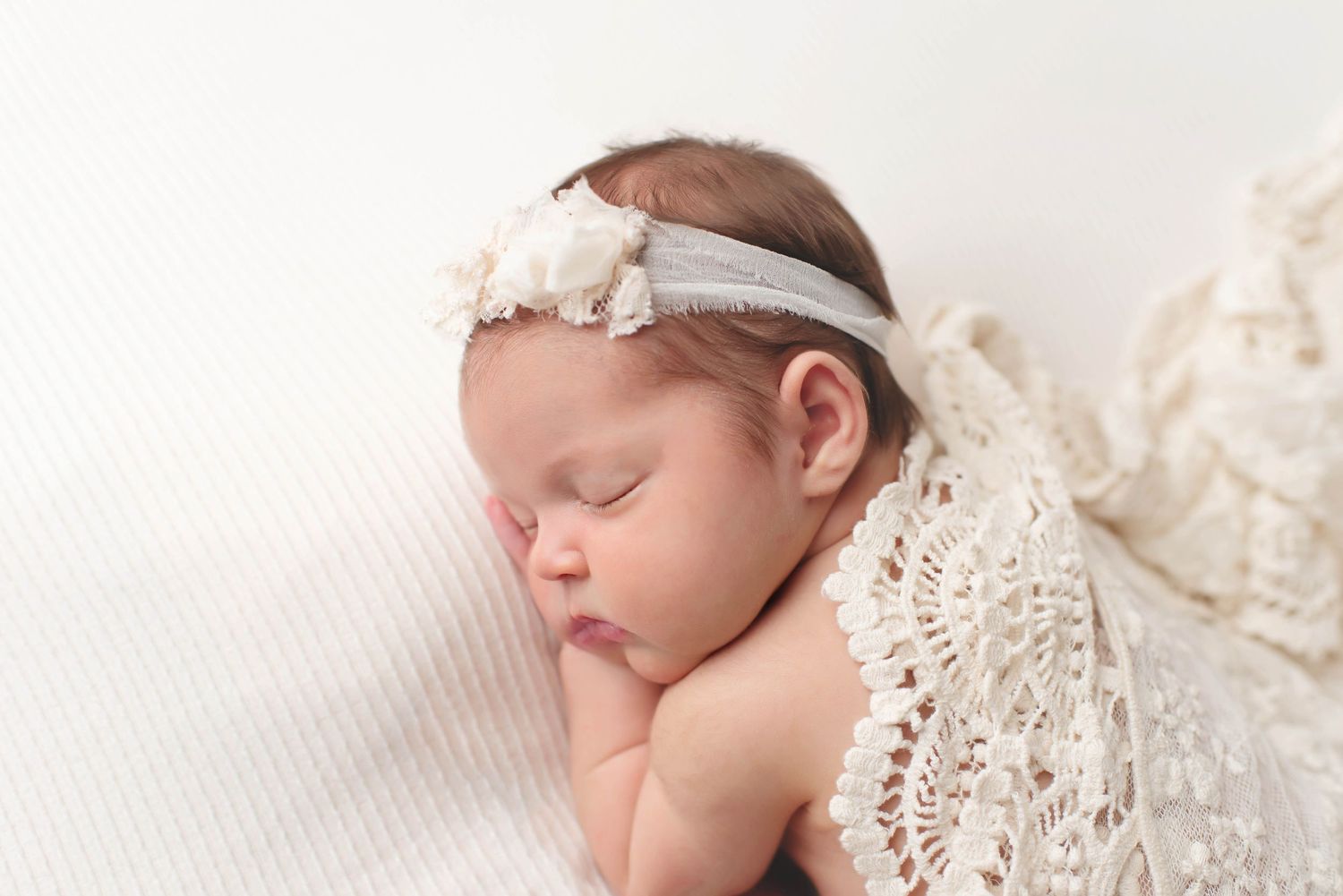 newborn baby girl on cream tan backdrop with boho lace wrap