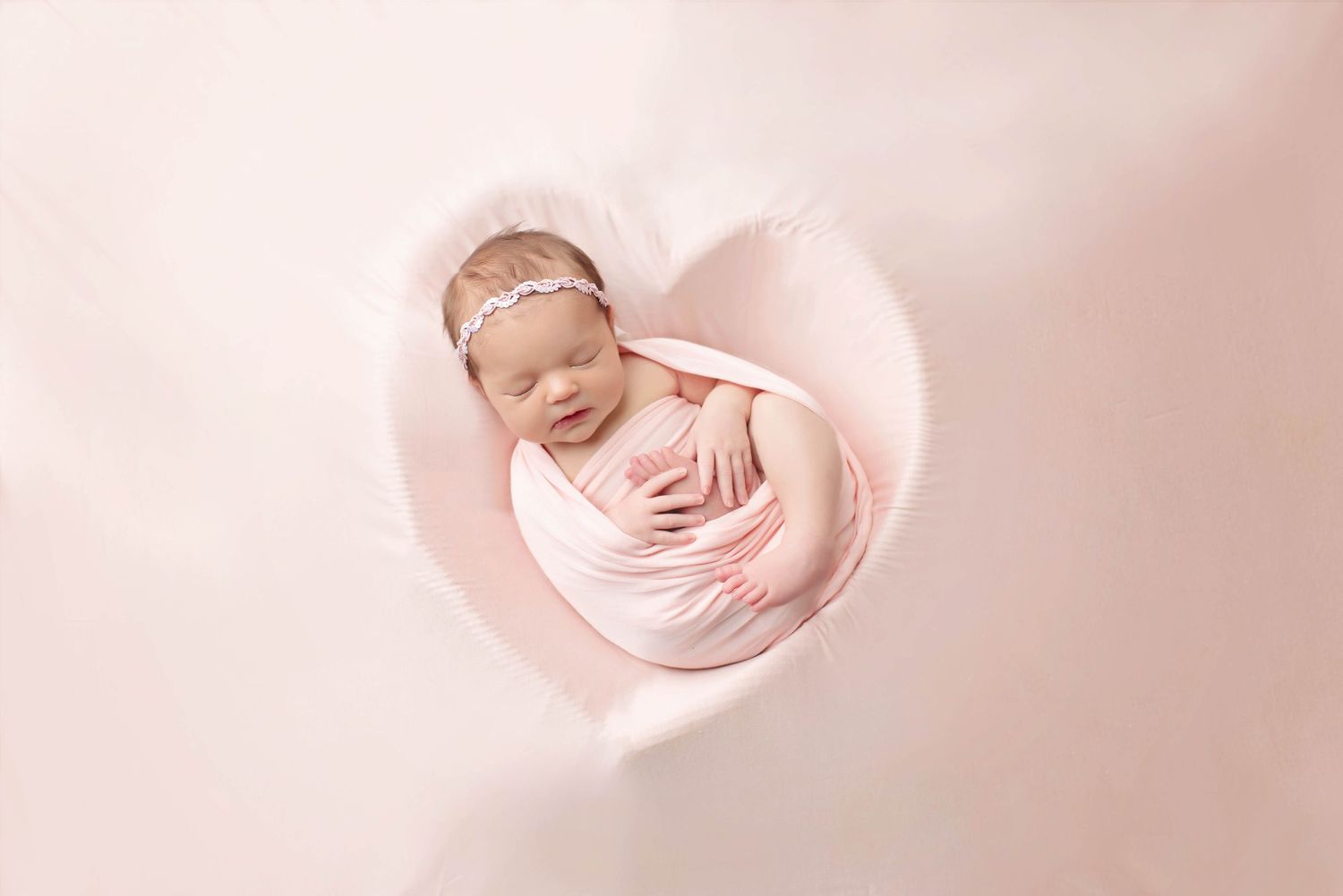 newborn baby girl in heart bowl with pink backdrop and wrap