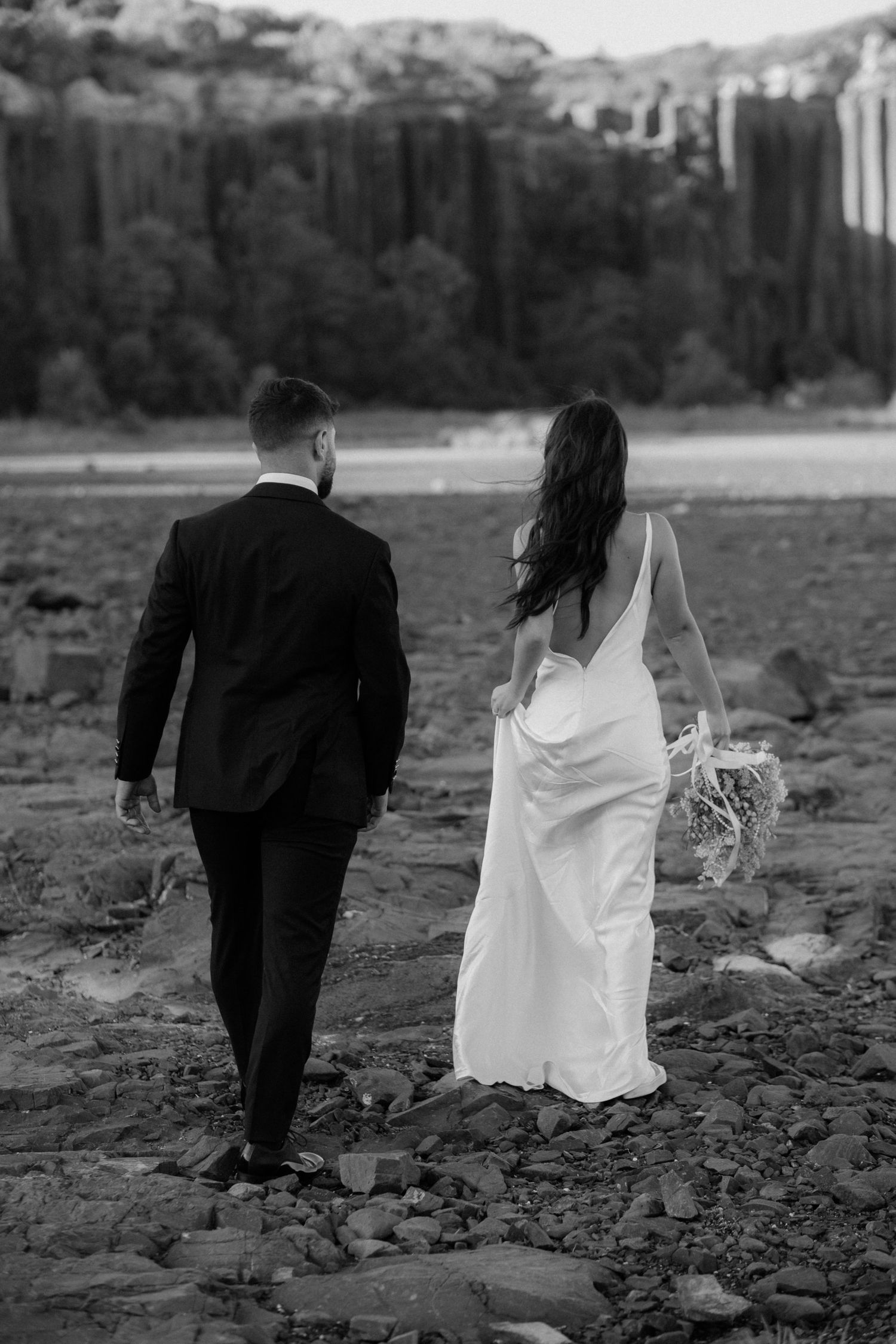 Couple walking across rocky terrain with towering cliffs in background.