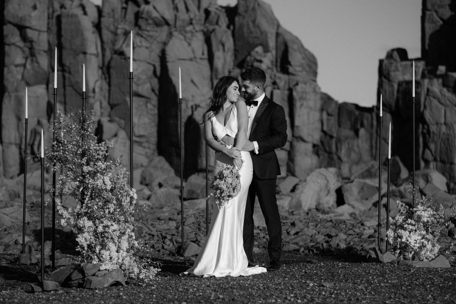 Wedding couple posing elegantly against dramatic cliff backdrop with floral decor.