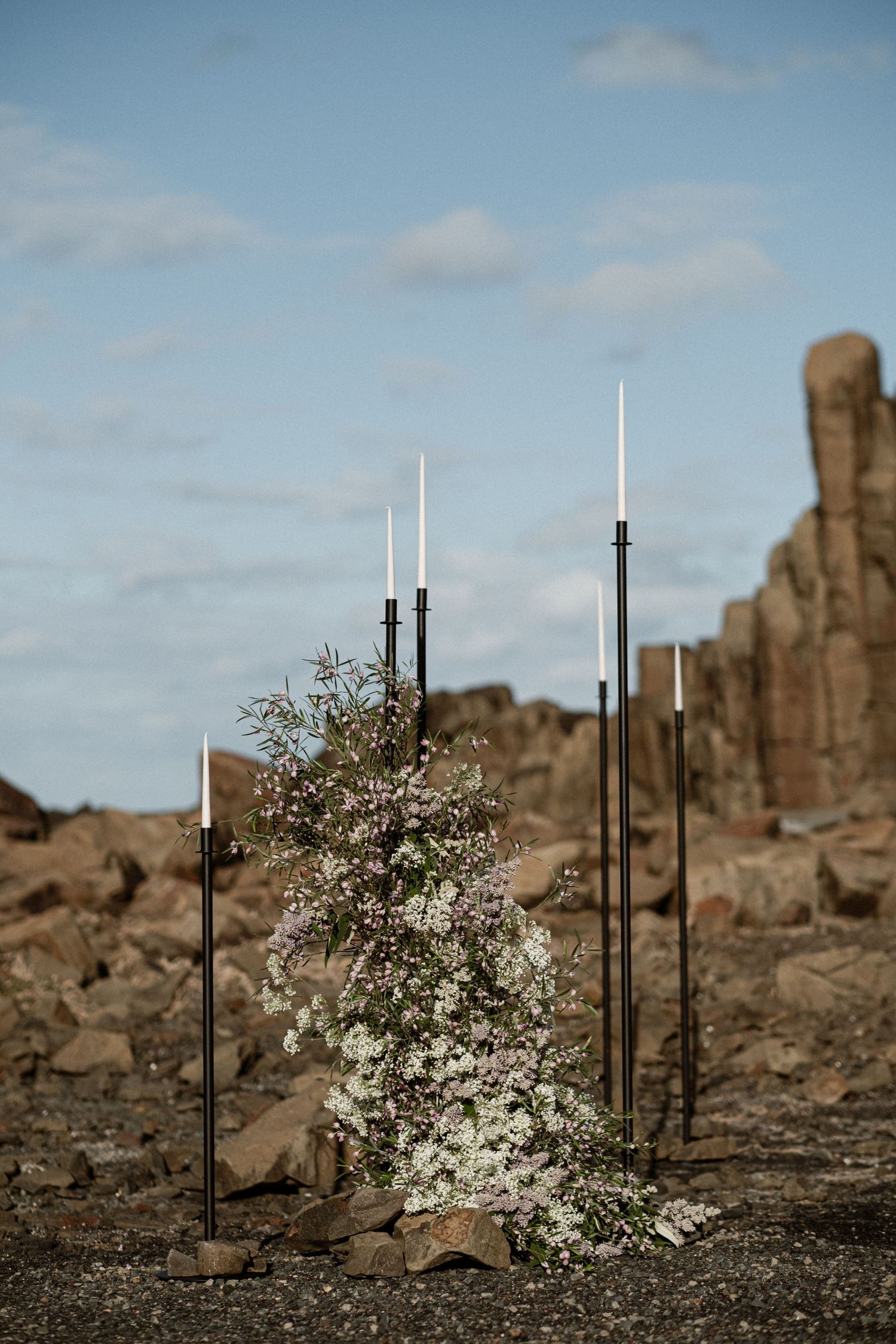 Modern white flower arrangement with black poles against desert rock formations under blue sky.