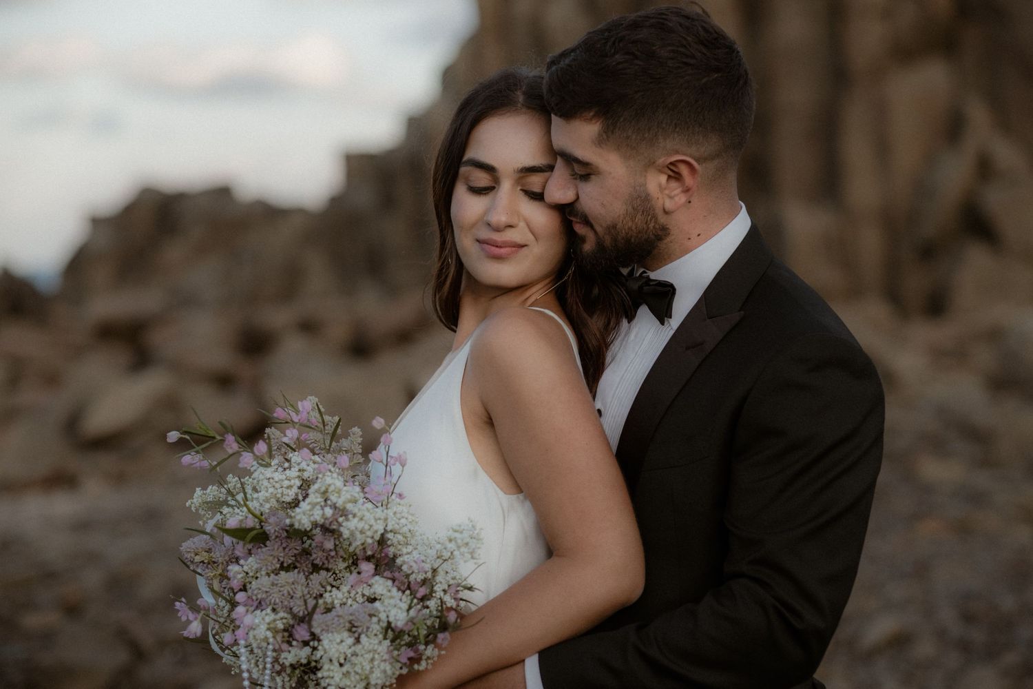Intimate wedding moment captured against rugged desert landscape with delicate bouquet.