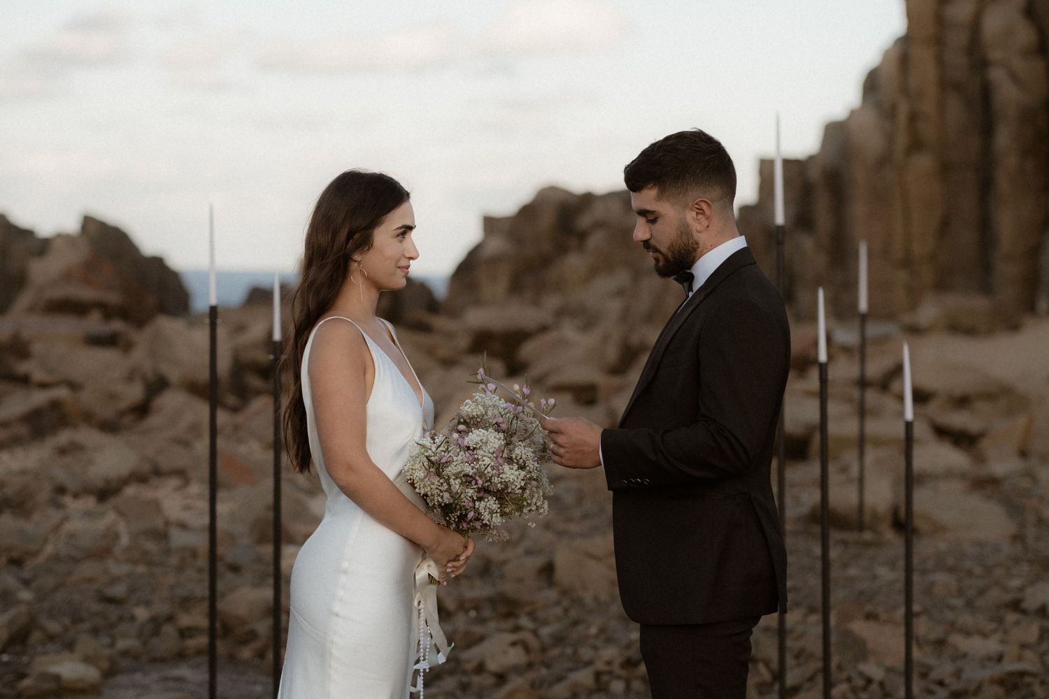 Intimate desert wedding ceremony with modern black poles and natural rock formations.