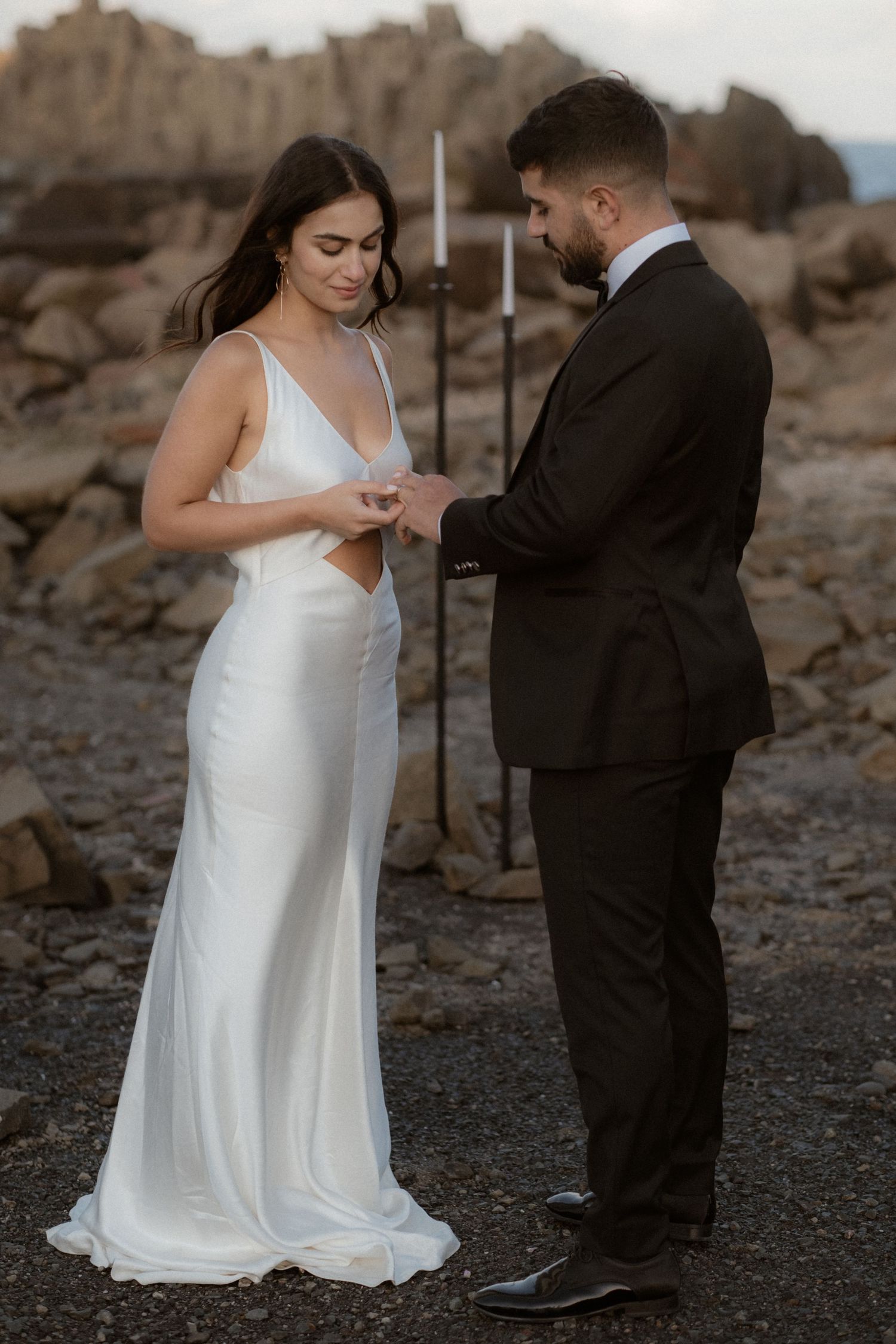 Wedding ring exchange ceremony against dramatic desert backdrop with vertical poles.