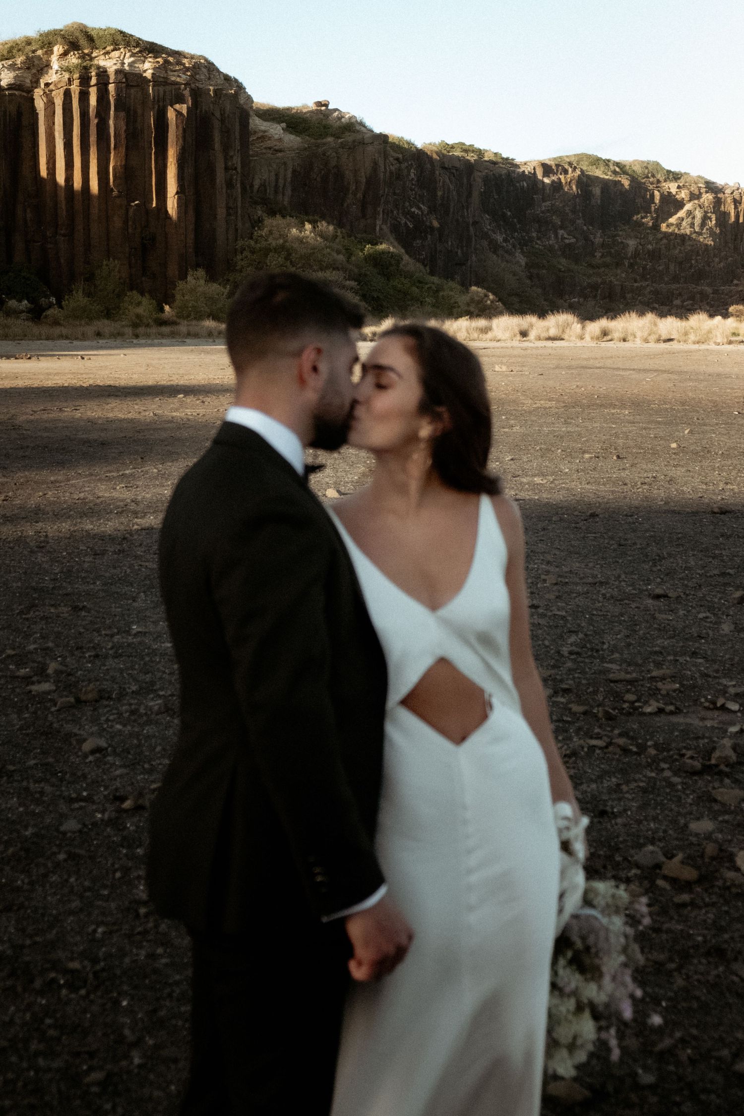 Modern wedding portrait with dramatic desert cliffs and intimate moment.