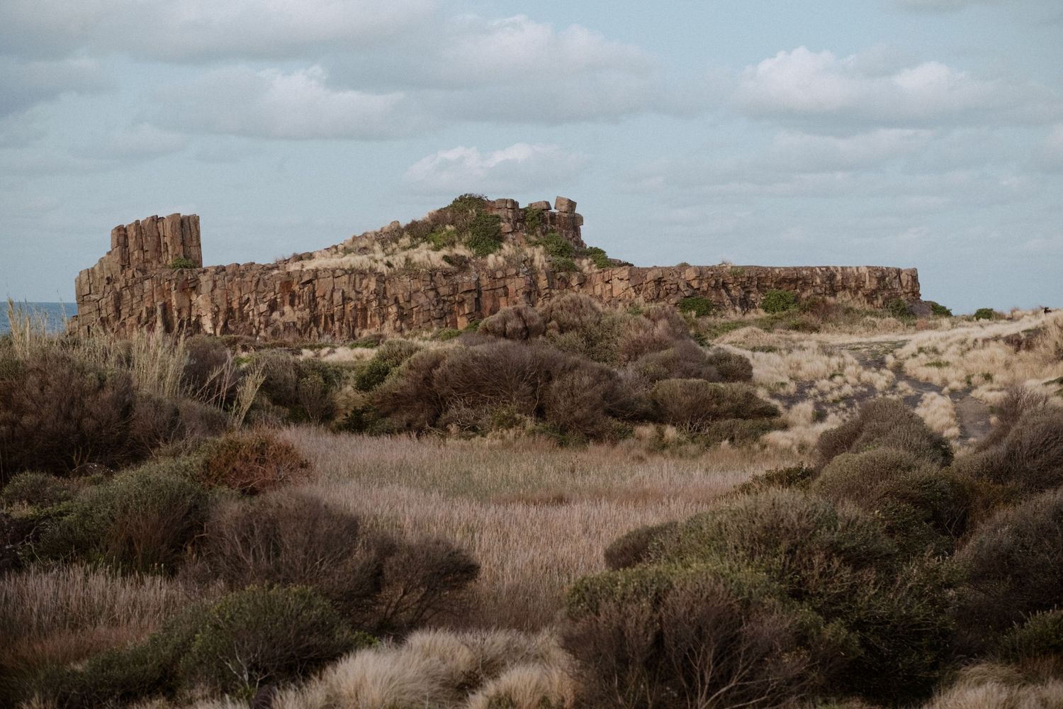 Rocky cliff formations and rugged terrain under cloudy skies in a desert landscape.