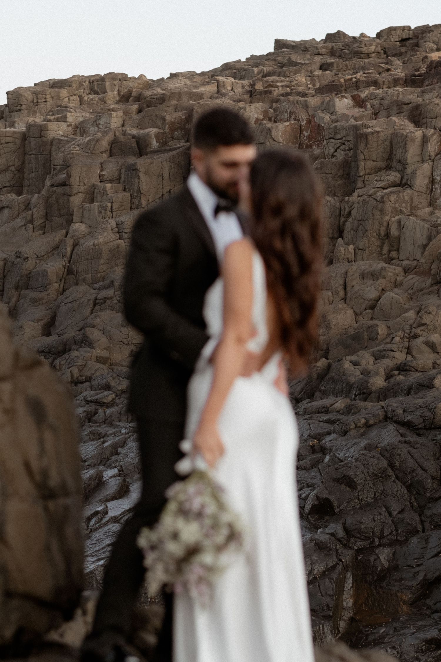 Intimate wedding portrait against dramatic rocky cliff backdrop.
