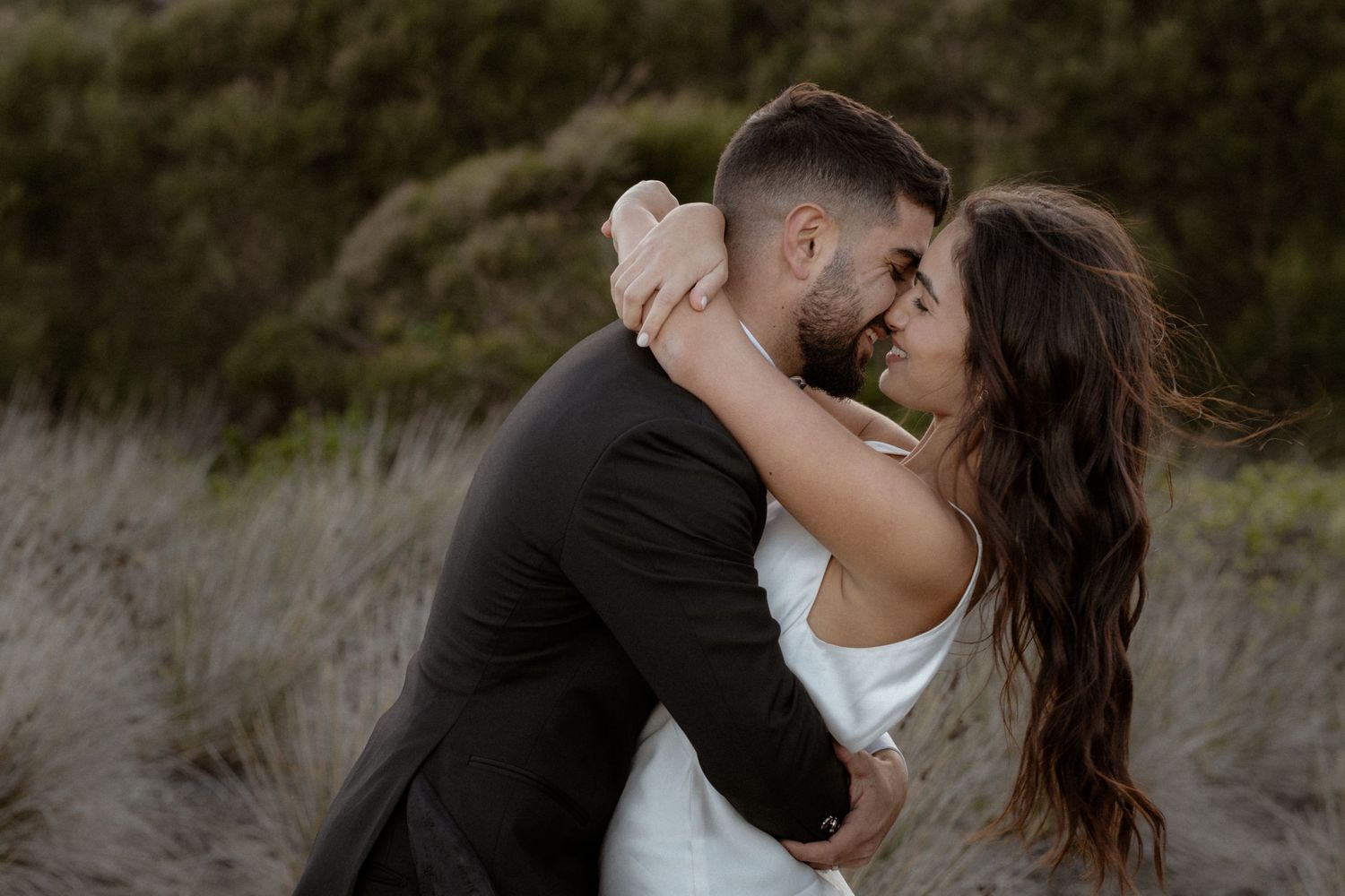 Intimate wedding portrait of couple in black and white attire against natural backdrop.