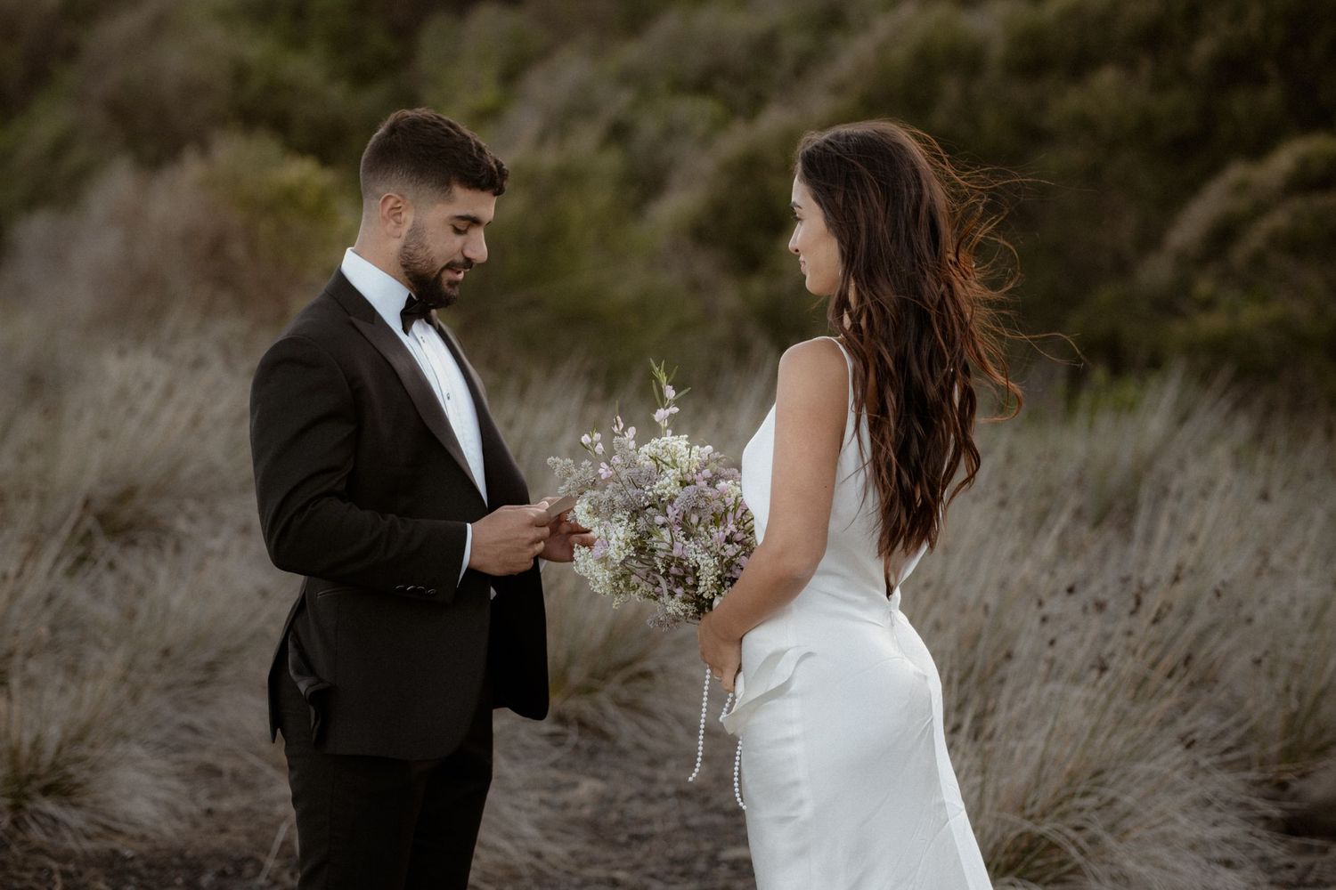 Wedding couple exchanges vows in natural outdoor setting with delicate bouquet.