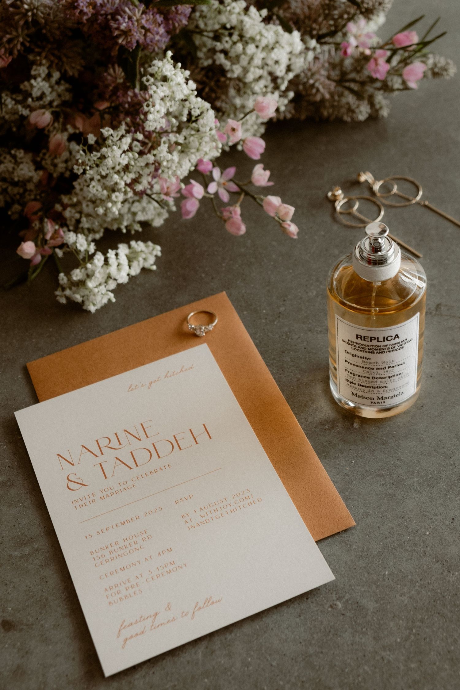 Wedding invitation with floral decorations and perfume bottle on grey surface.