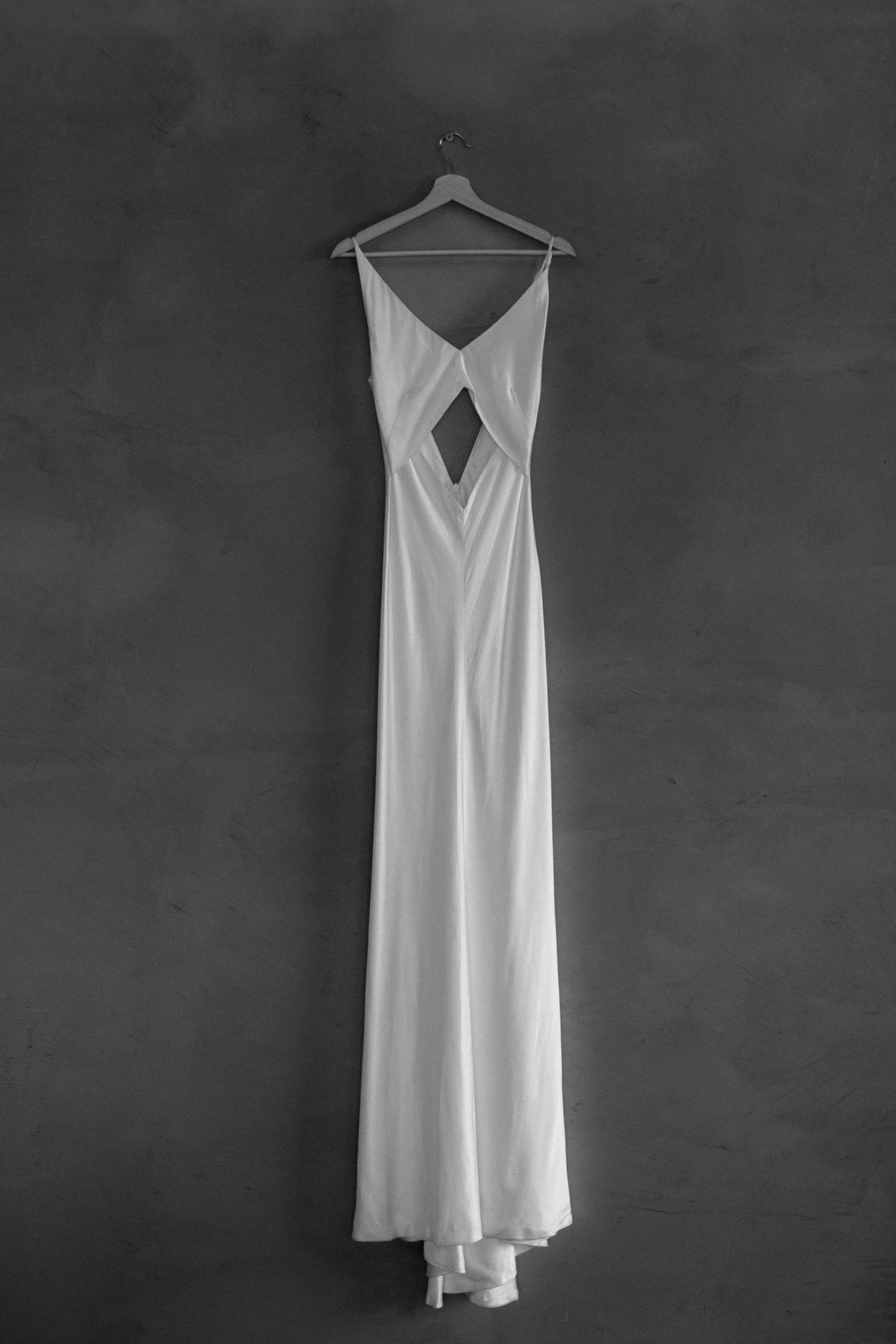 Elegant white wedding dress with cutout detail hanging against dark background.