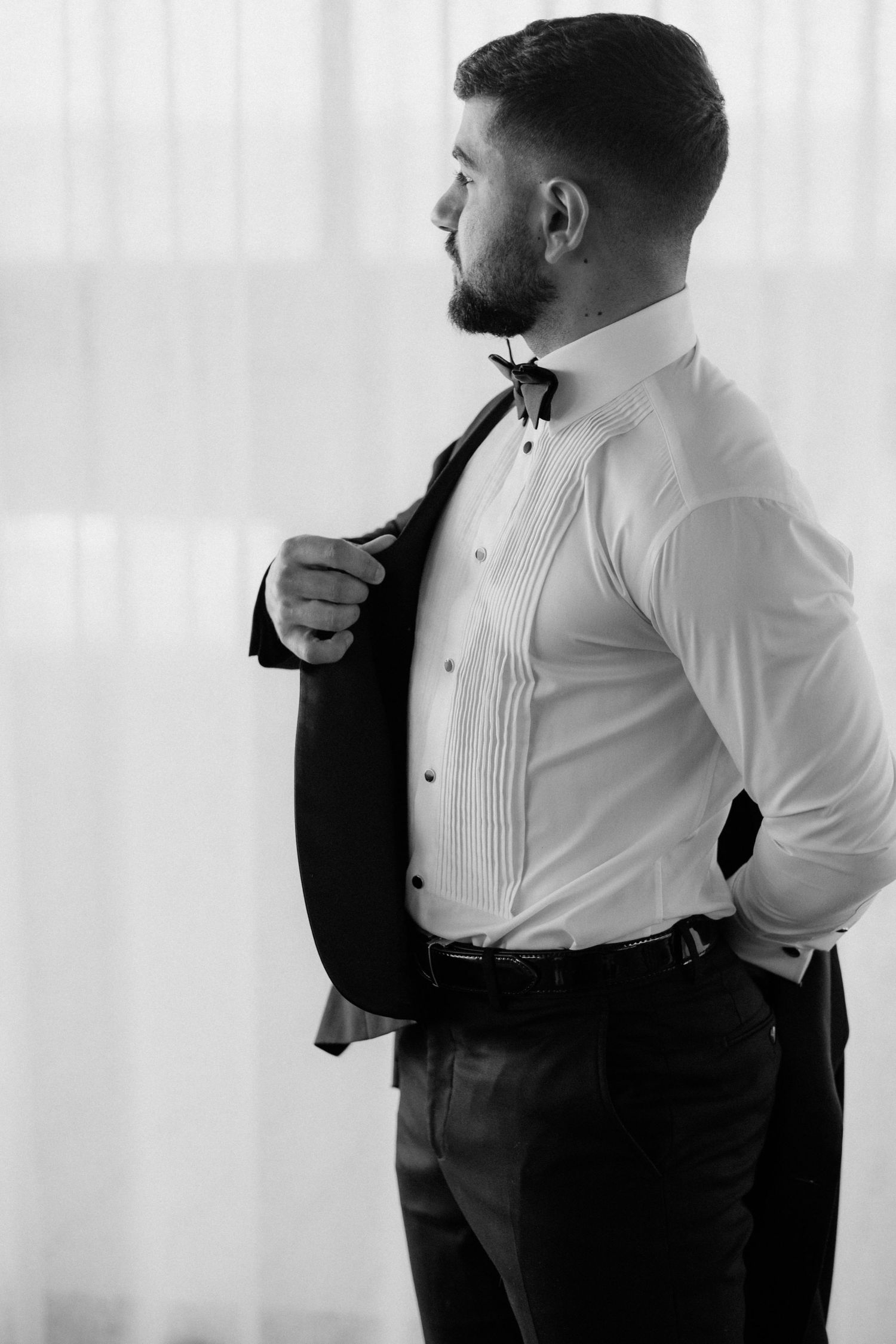 Side profile of man in tuxedo shirt and bow tie adjusting his formal wear.