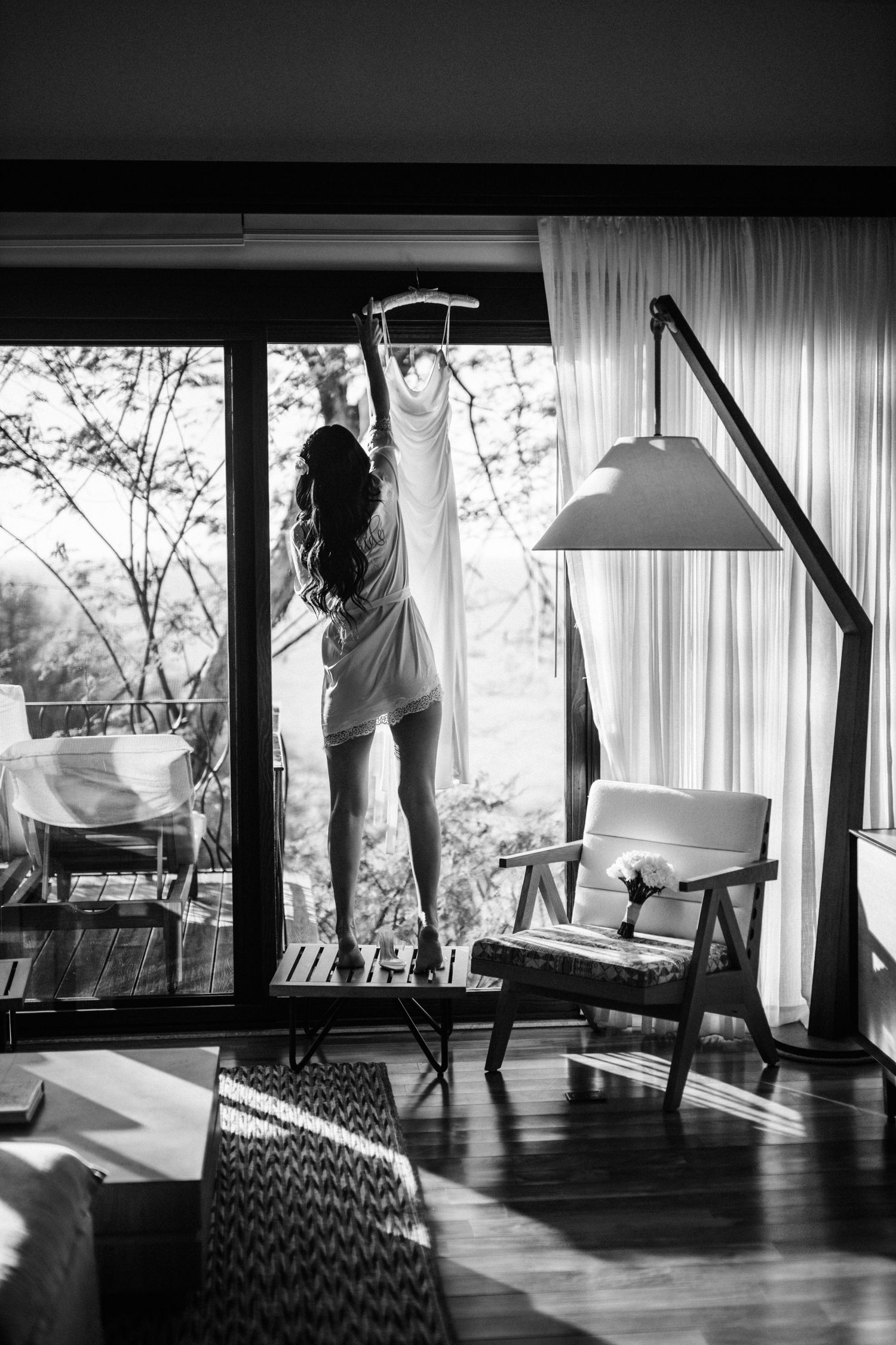 Silhouette of a person stretching by large windows in a modern room with floor lamp.