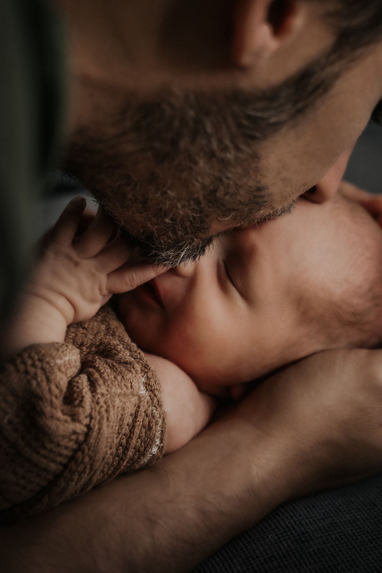 Close-up intimate moment between parent and infant wrapped in brown knit fabric.