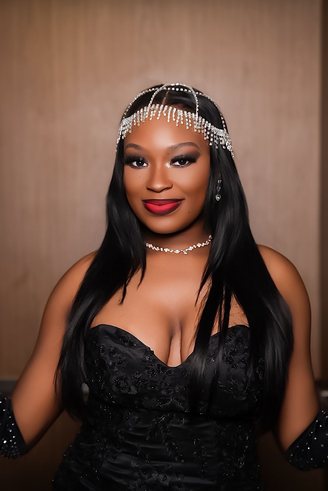 Woman in a black beaded gown with a sparkling crystal headpiece, red lipstick, and long straight black hair poses elegantly.