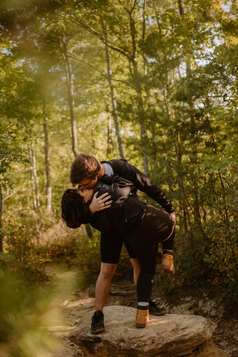 A man dips his partner in an embrace in the middle of a forest path on a sunny day.