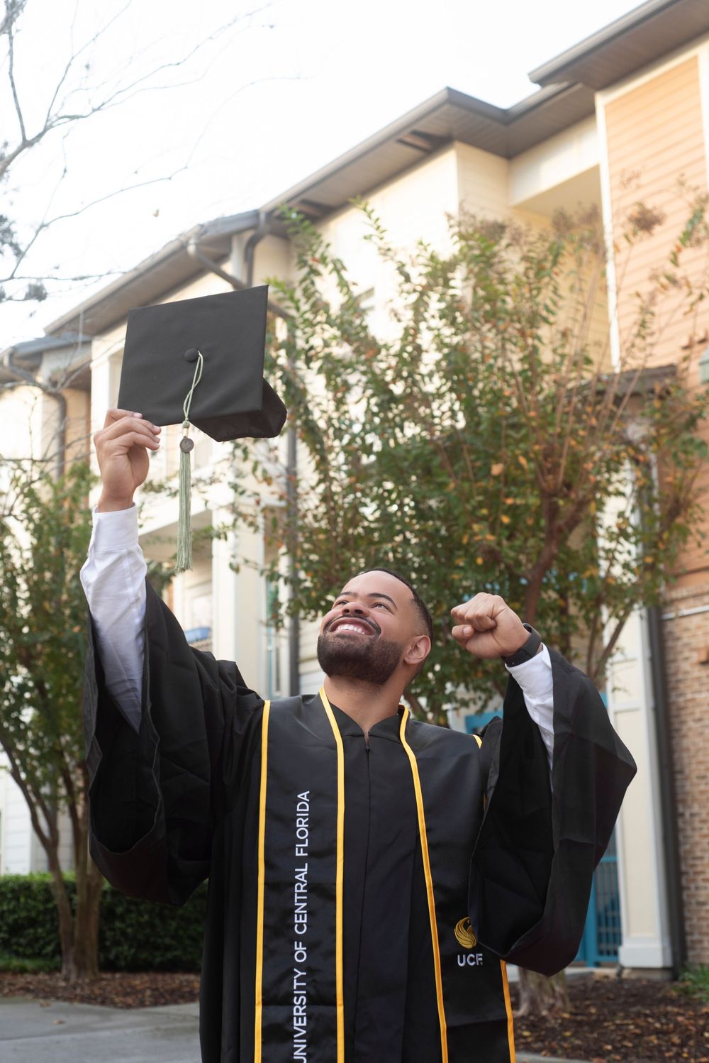 Solo male senior college grad session cap and gown excitement. Soft morning natural lighting at Oviedo on the Park in Oveido Florida