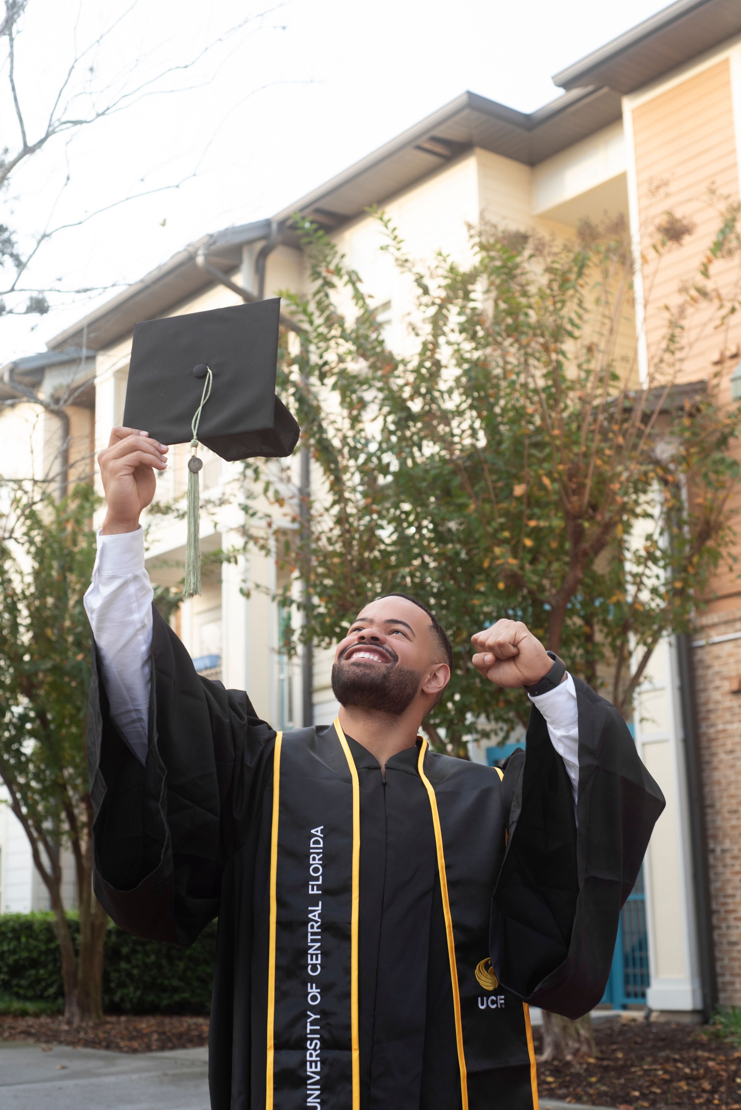 Solo male senior college grad session cap and gown excitement. Soft morning natural lighting at Oviedo on the Park in Oveido Florida