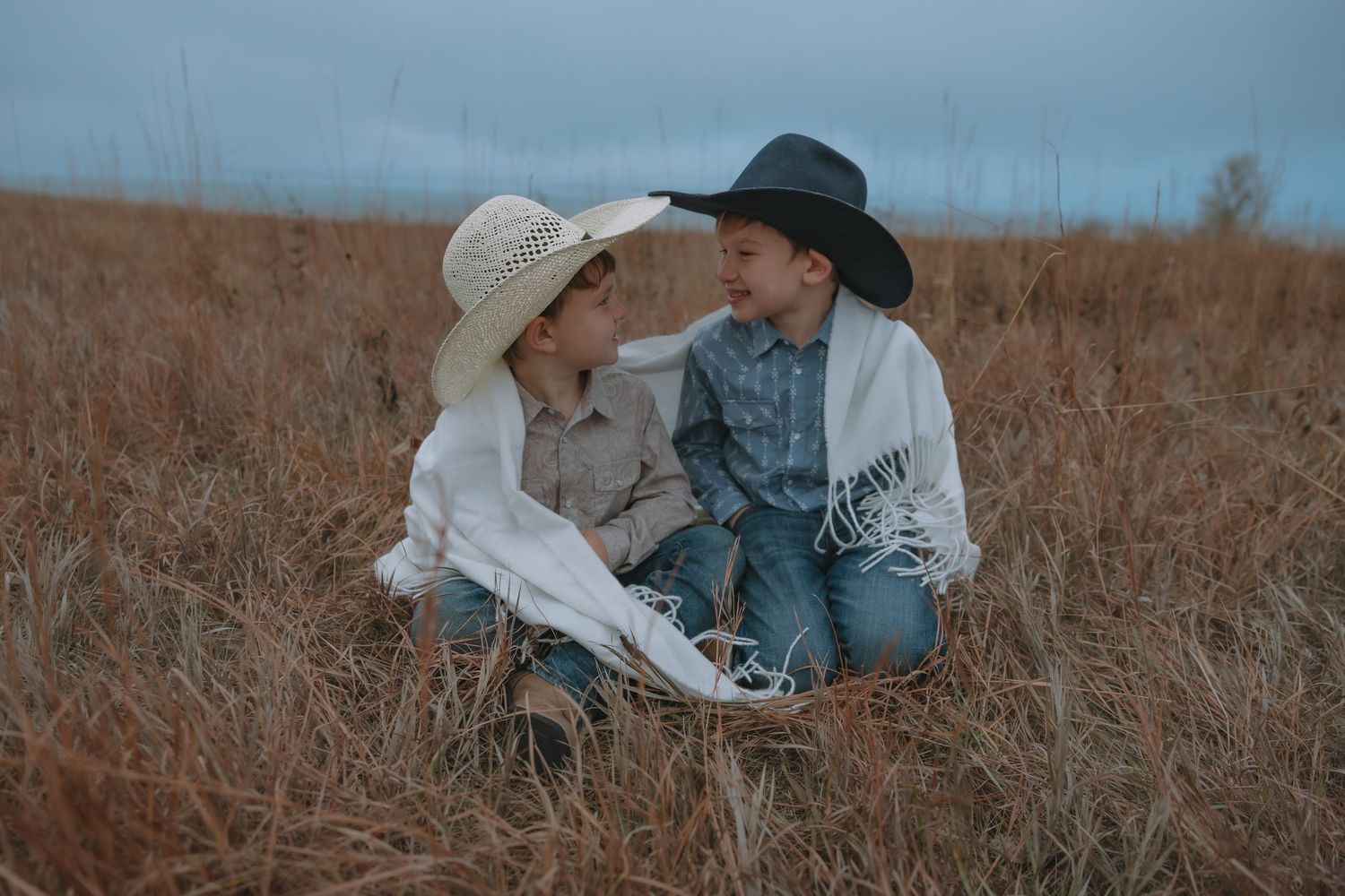 Garrison ND family portrait of two little boys in cowboy style clothing sitting on hillside above Lake Sakakawea wrapped in a blanket