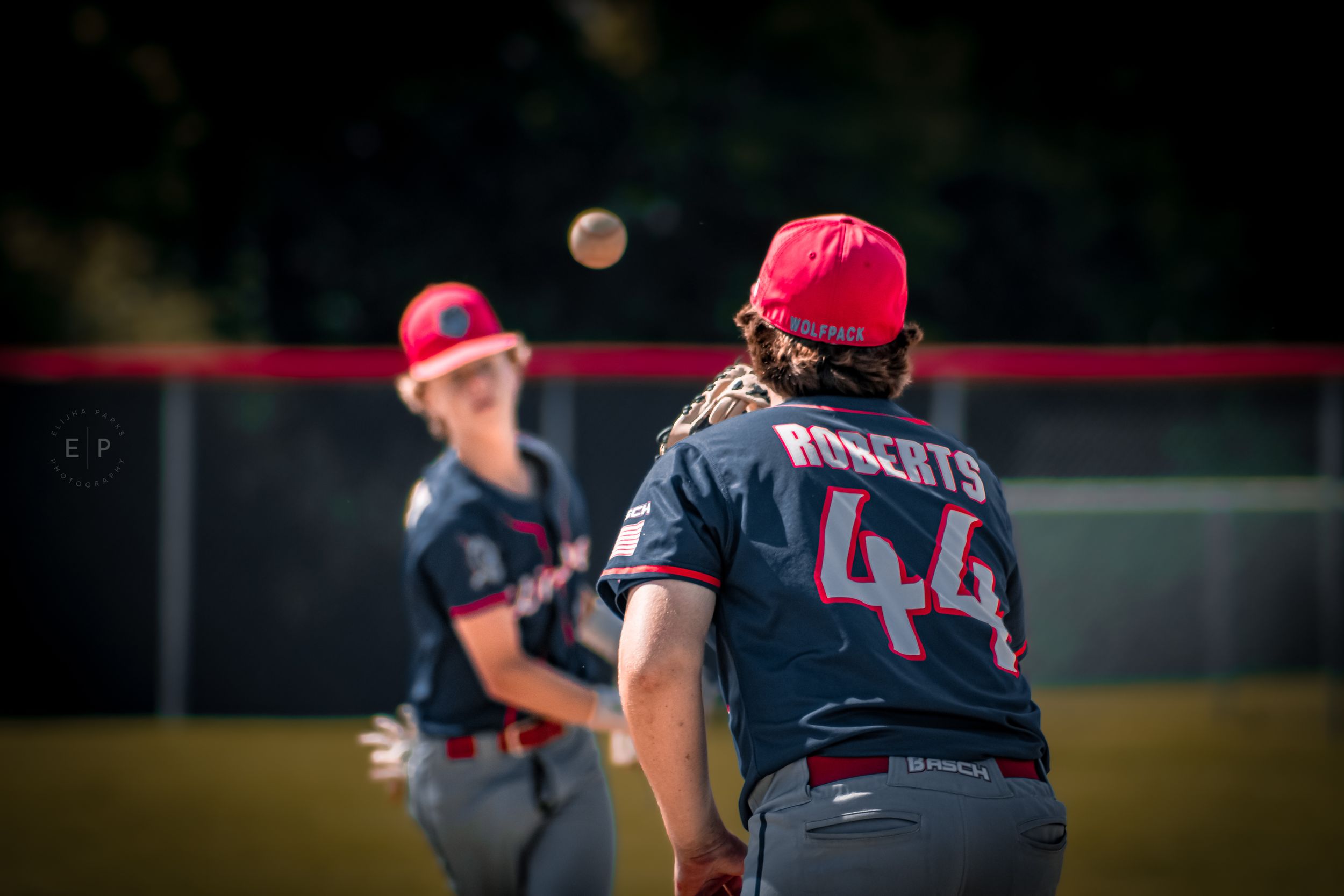 One baseball player facing teammate awaiting thrown baseball.