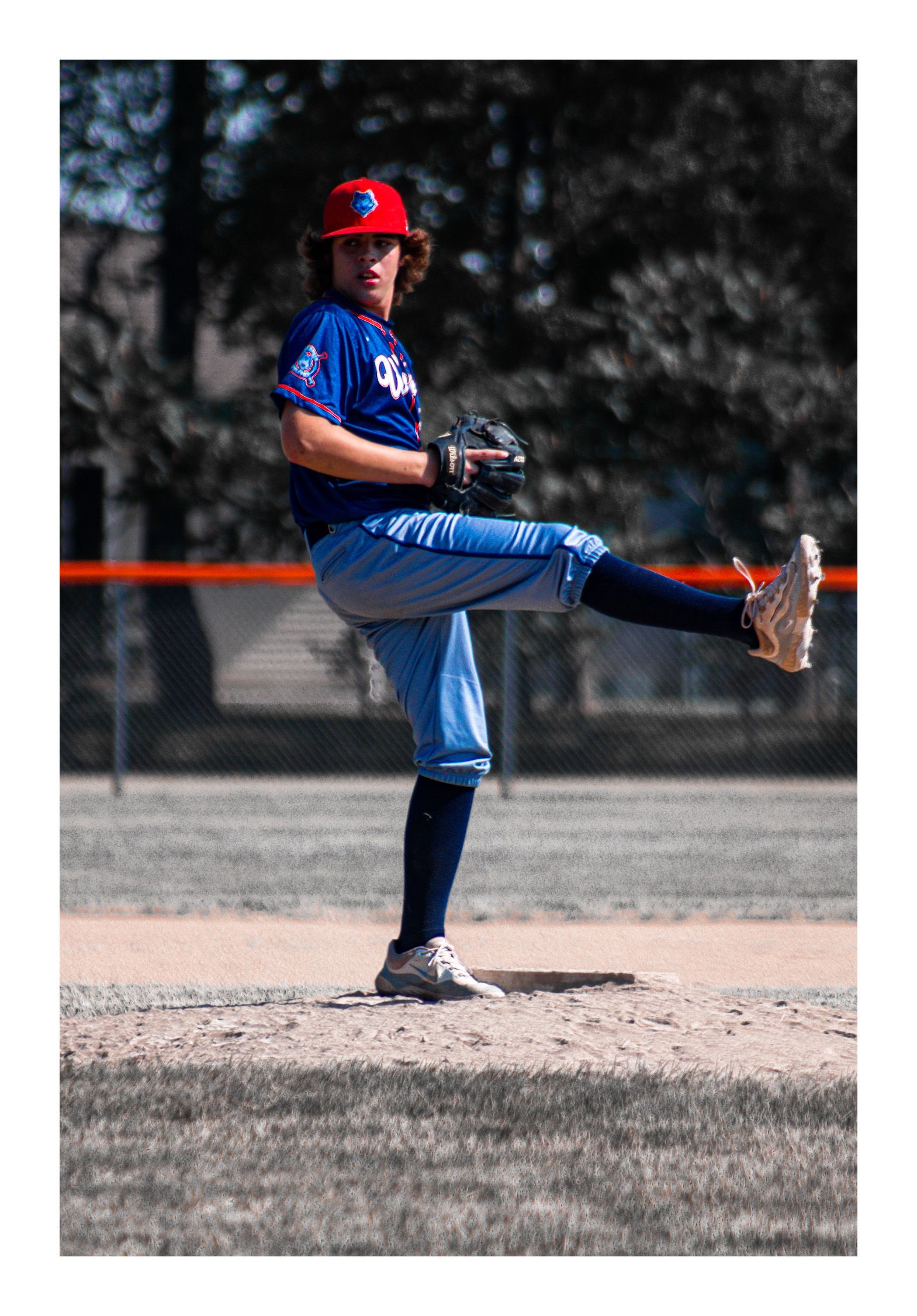 Baseball pitcher on pitchers mound, preparing to pitch ball with leg up and head toward home plate