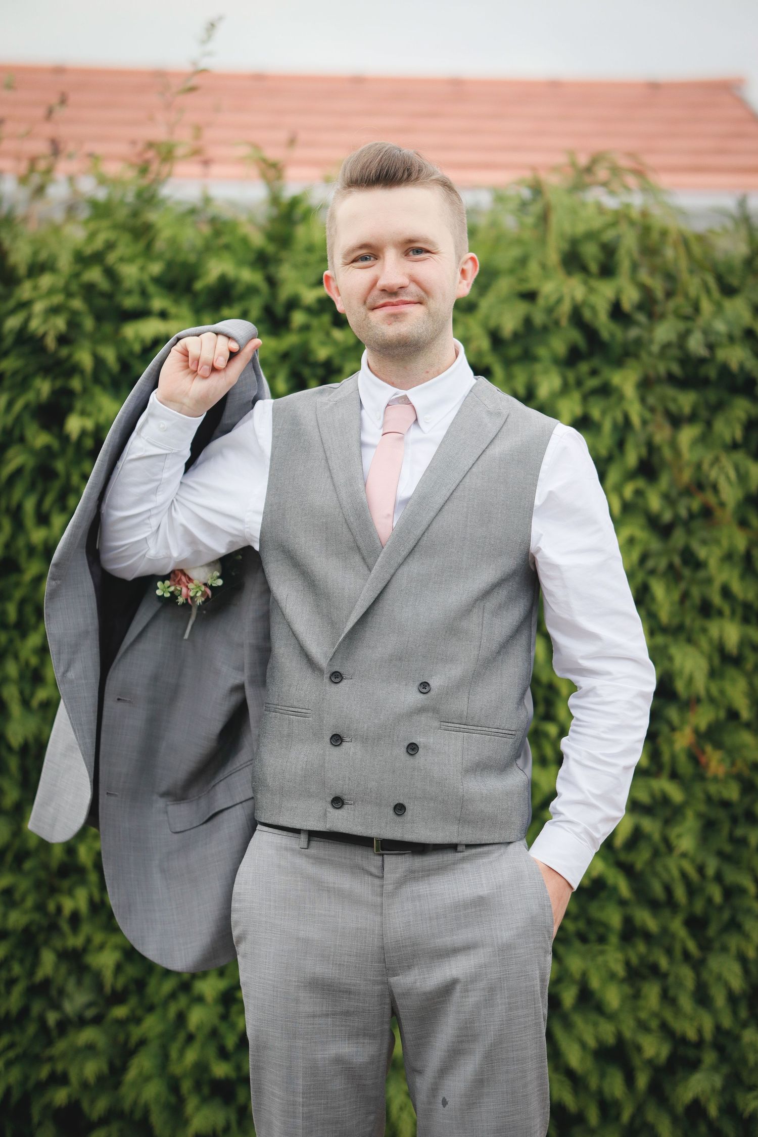 Groom in gray vest and white shirt poses confidently outdoors.