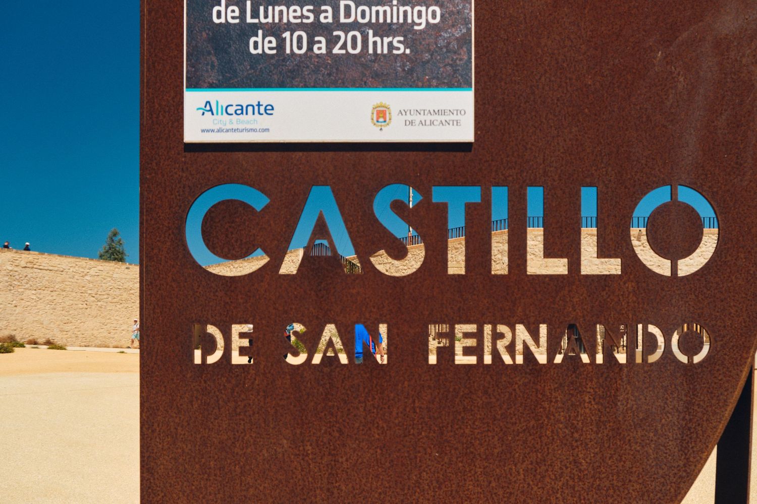 Brown sign displaying 'Castillo de San Fernando' against blue sky.