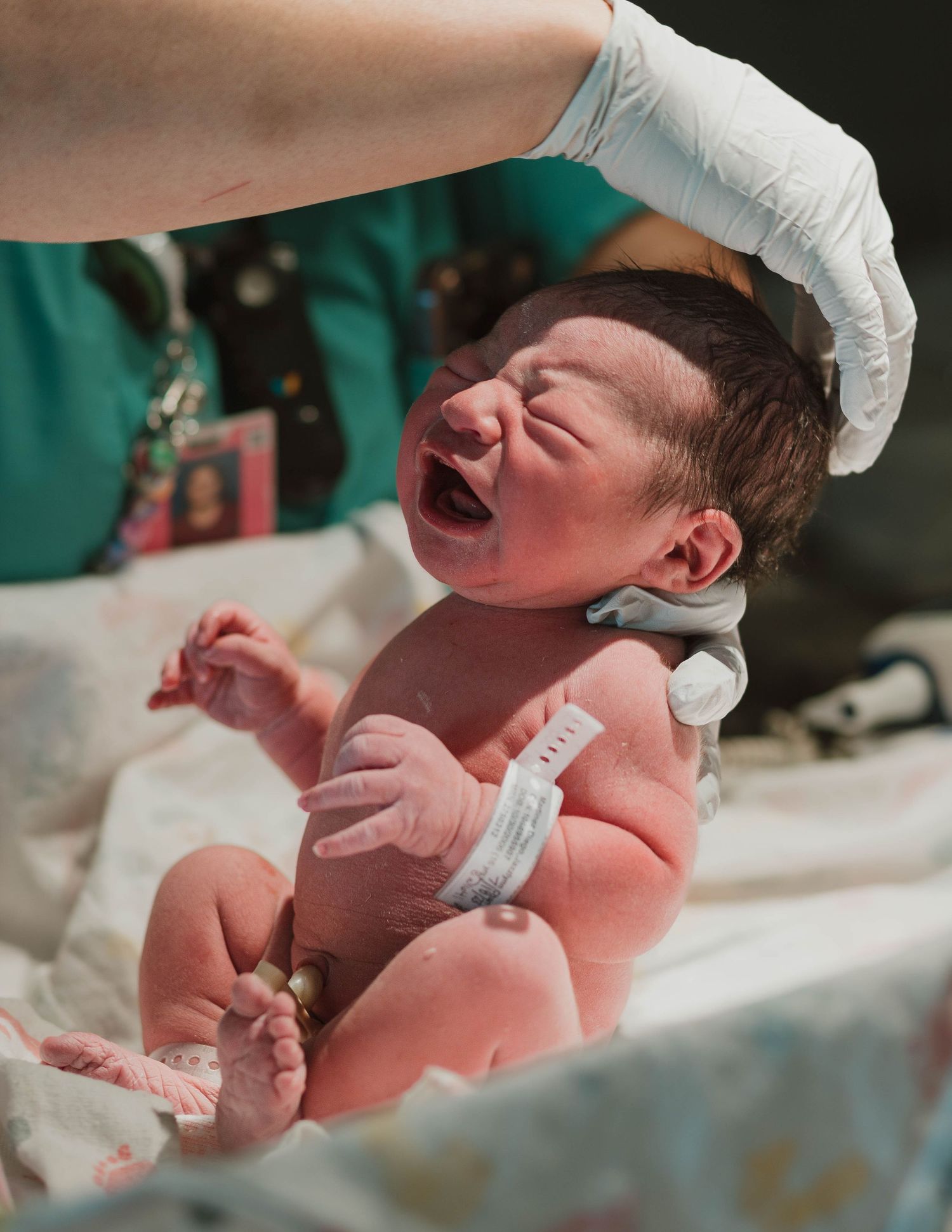 Newborn baby crying during first medical examination with hospital staff in background.