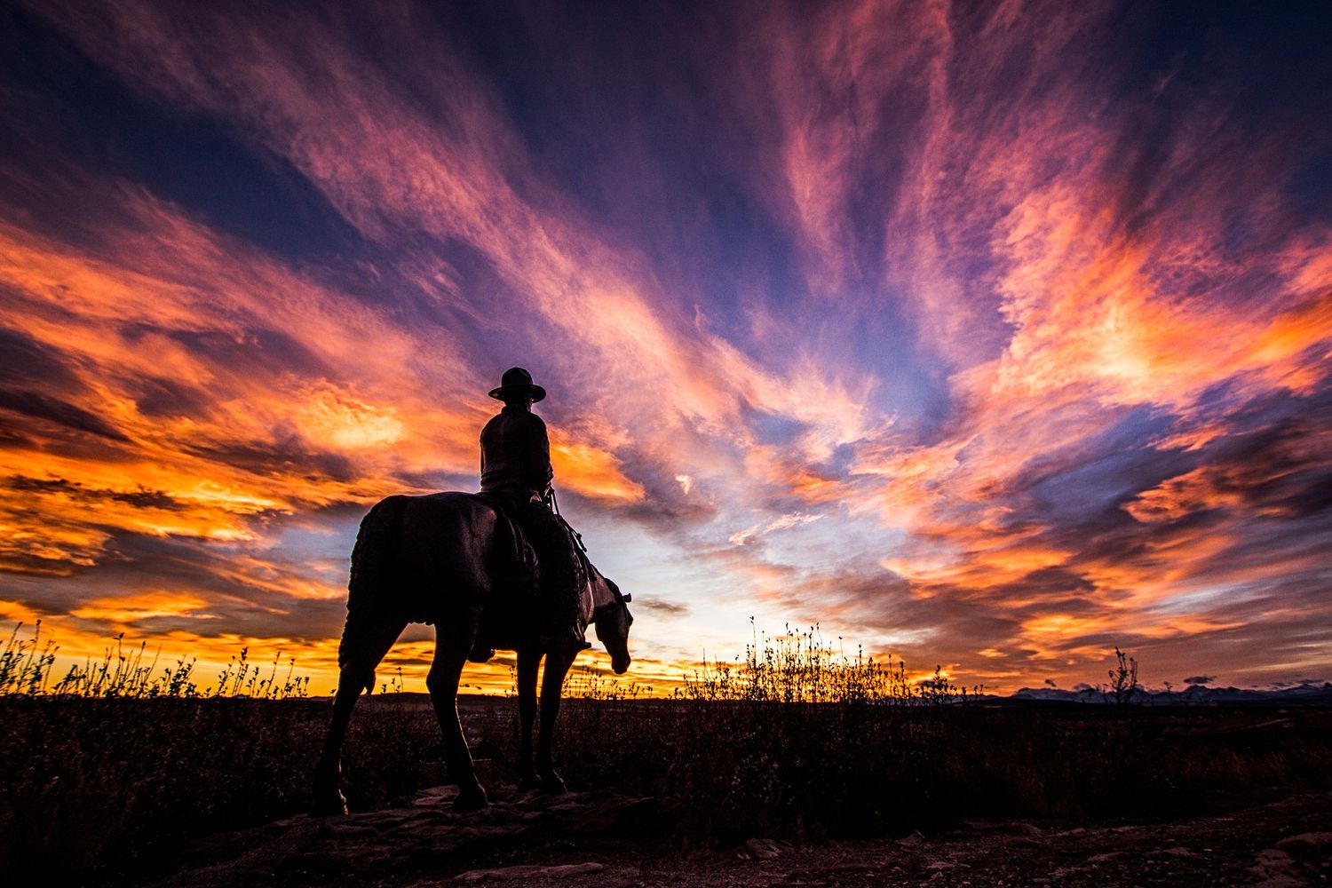 Silhouette of a cowboy on horseback beneath a dramatic fiery sunset sky.