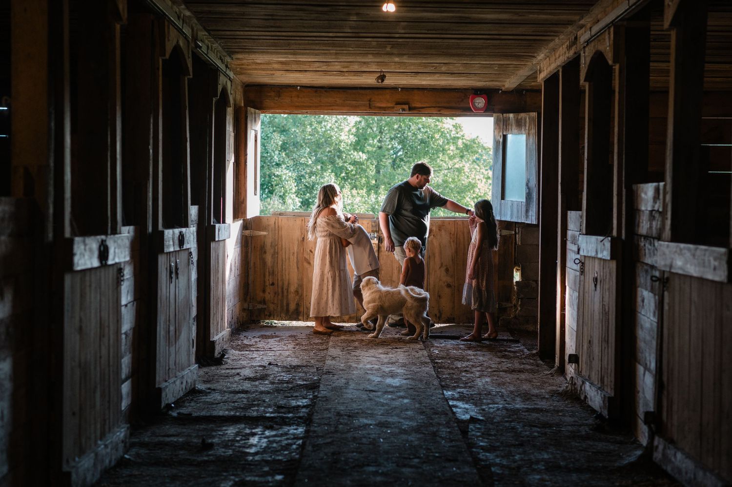 People standing in rustic wooden horse stable corridor.
