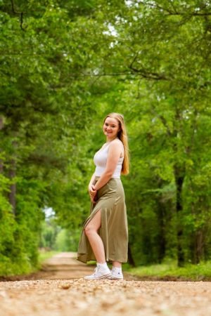 A person poses on a forest trail wearing a white top and long beige skirt with a side slit.