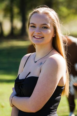 A person in a black top smiles warmly while standing outdoors on a sunny day.