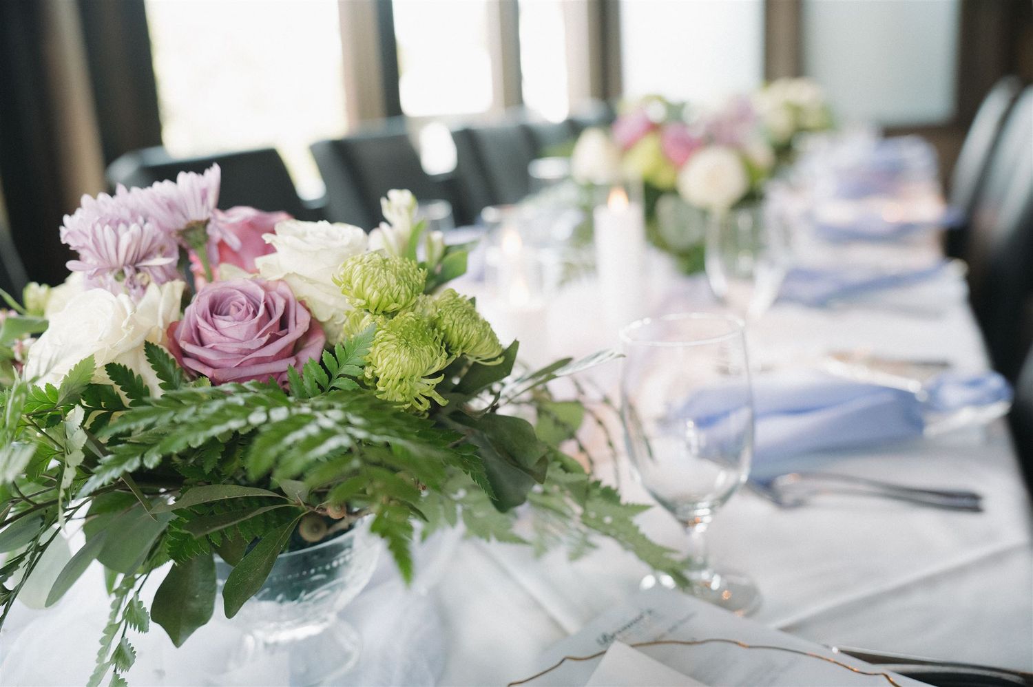 Pastel rose and greenery centerpiece decorates elegant wedding table with soft blue accents.